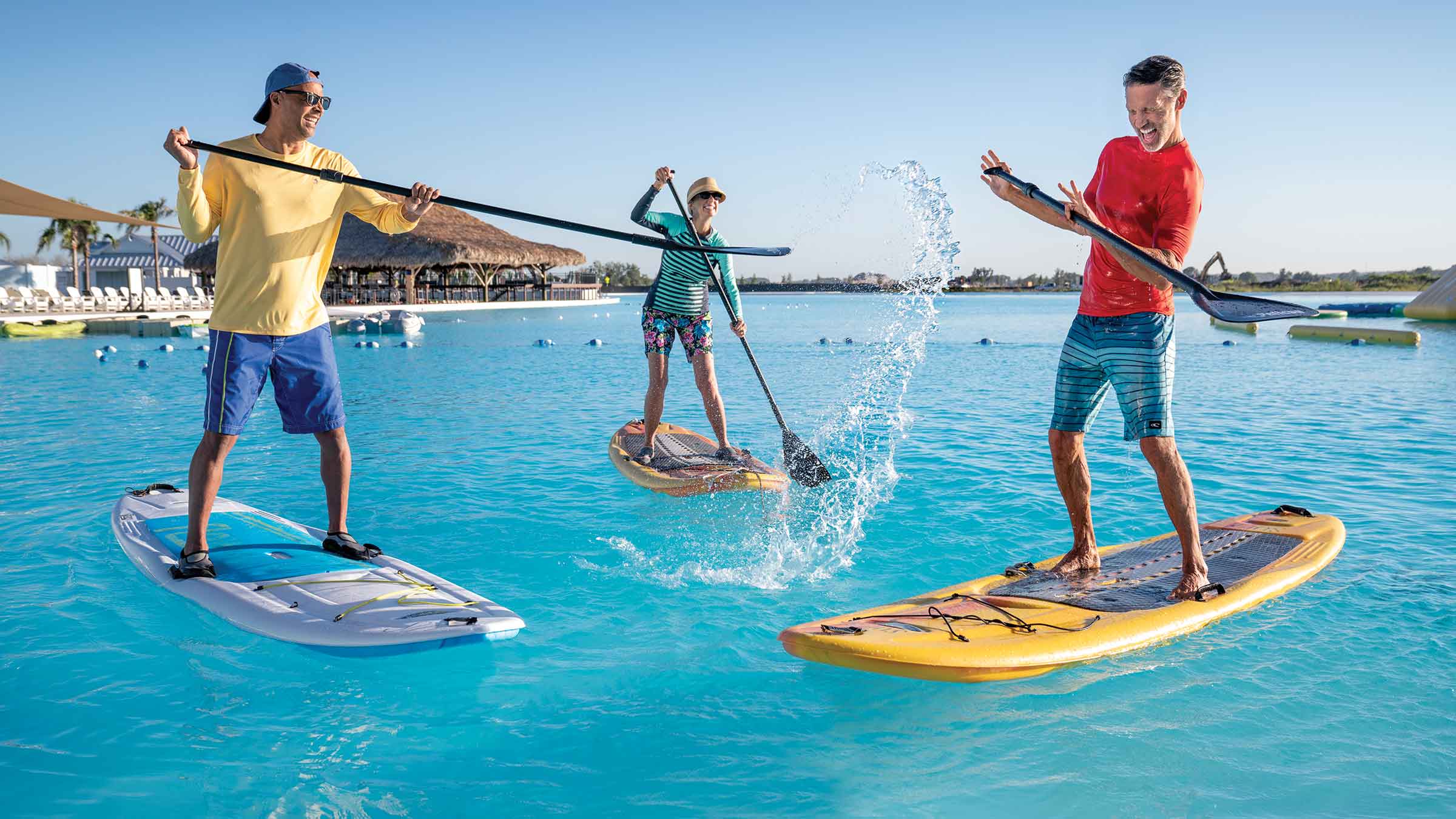 Three adults splashing each other on standup paddleboards on a Metro Lagoon