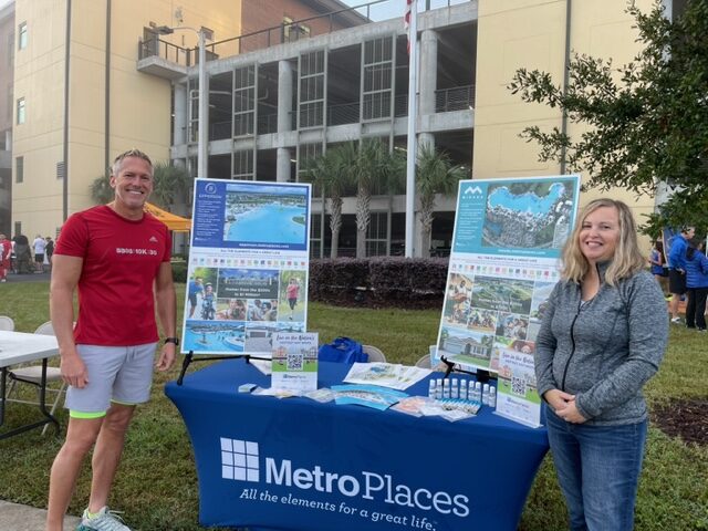 Image of John and Vicky, members of MetroPlaces’ marketing team, working our booth at the 2021 5K Honor Run.