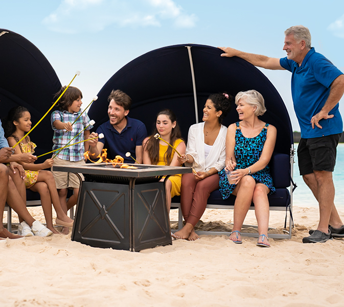 generational family sitting on beach around a fire making s'mores